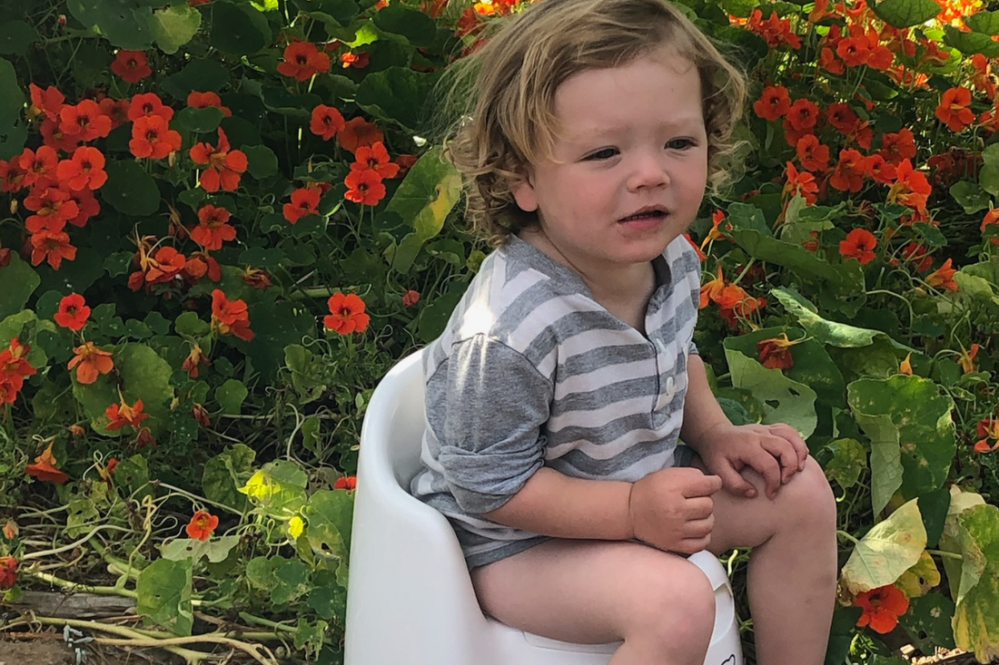 Photo of toddler using a potty in a yard with flowers. When the child is learning it is good to allow them to potty anywhere they are comfortable.